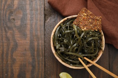 Tasty seaweed salad in bowl served on wooden table, flat lay. Space for text