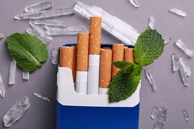 Photo of Pack of cigarettes, menthol crystals and mint leaves on grey background, flat lay