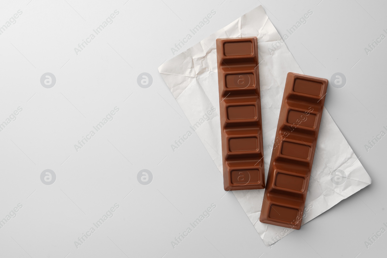 Photo of Paper wrap with delicious chocolate bars on light blue background, top view. Space for text