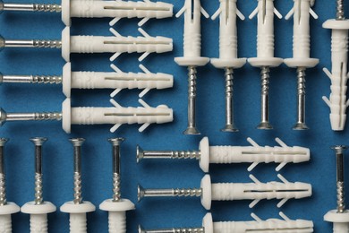 Many metal screws with white dowels on blue background, flat lay