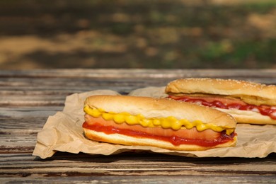 Photo of Fresh delicious hot dogs with sauces on wooden surface outdoors
