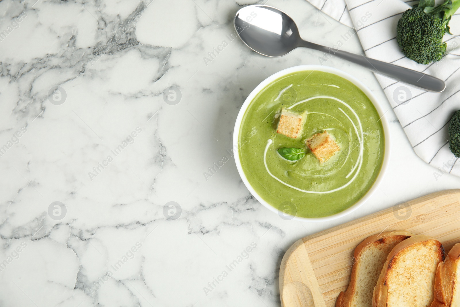 Photo of Delicious broccoli cream soup with croutons served on white marble table, flat lay. Space for text