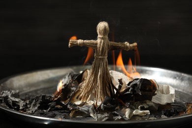 Voodoo doll burning in metal tray on dark background. Curse ceremony