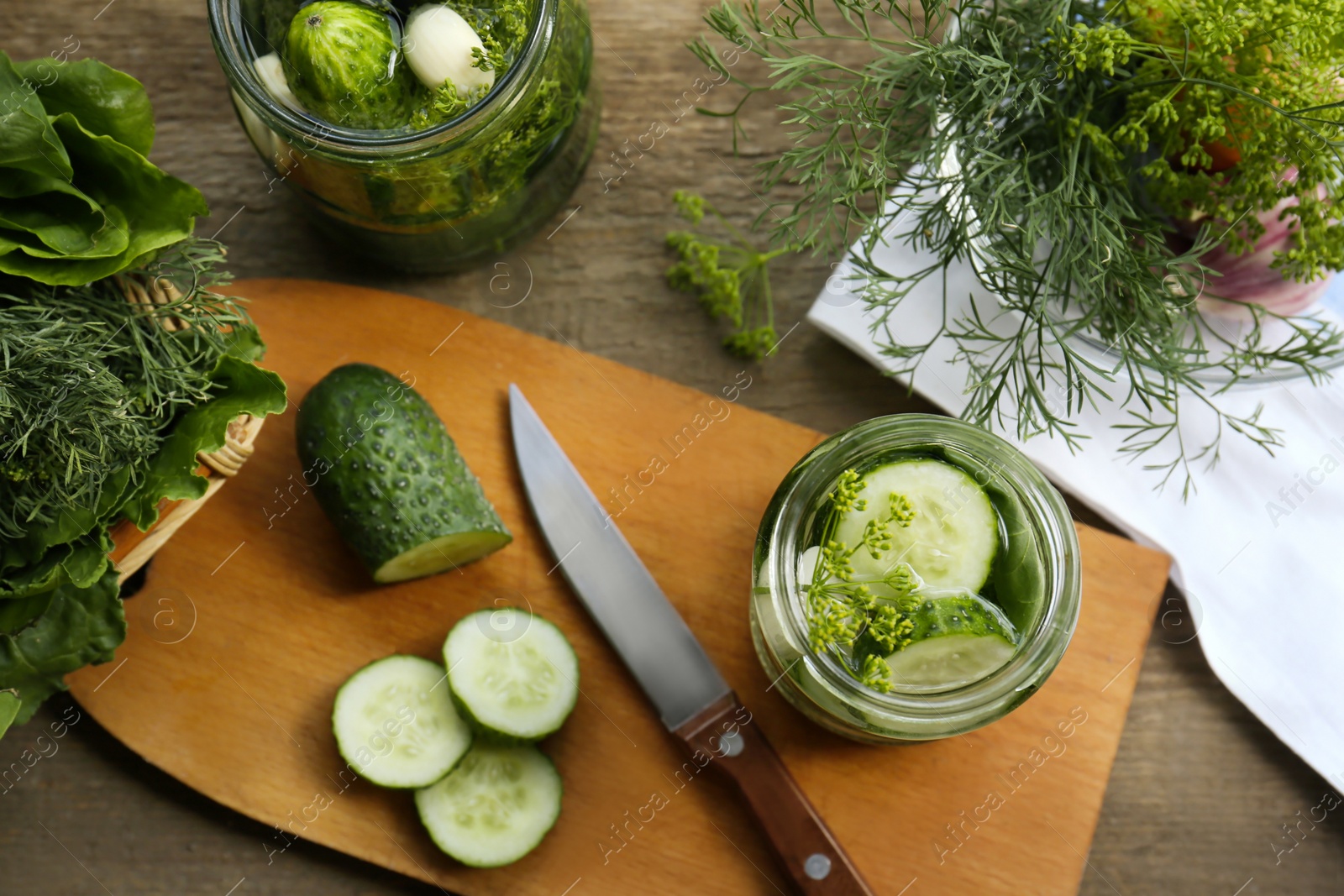 Photo of Glass jars, fresh cucumbers and herbs on wooden table, flat lay. Pickling recipe