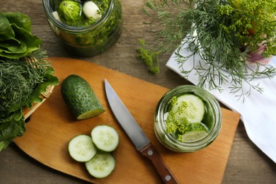 Photo of Glass jars, fresh cucumbers and herbs on wooden table, flat lay. Pickling recipe