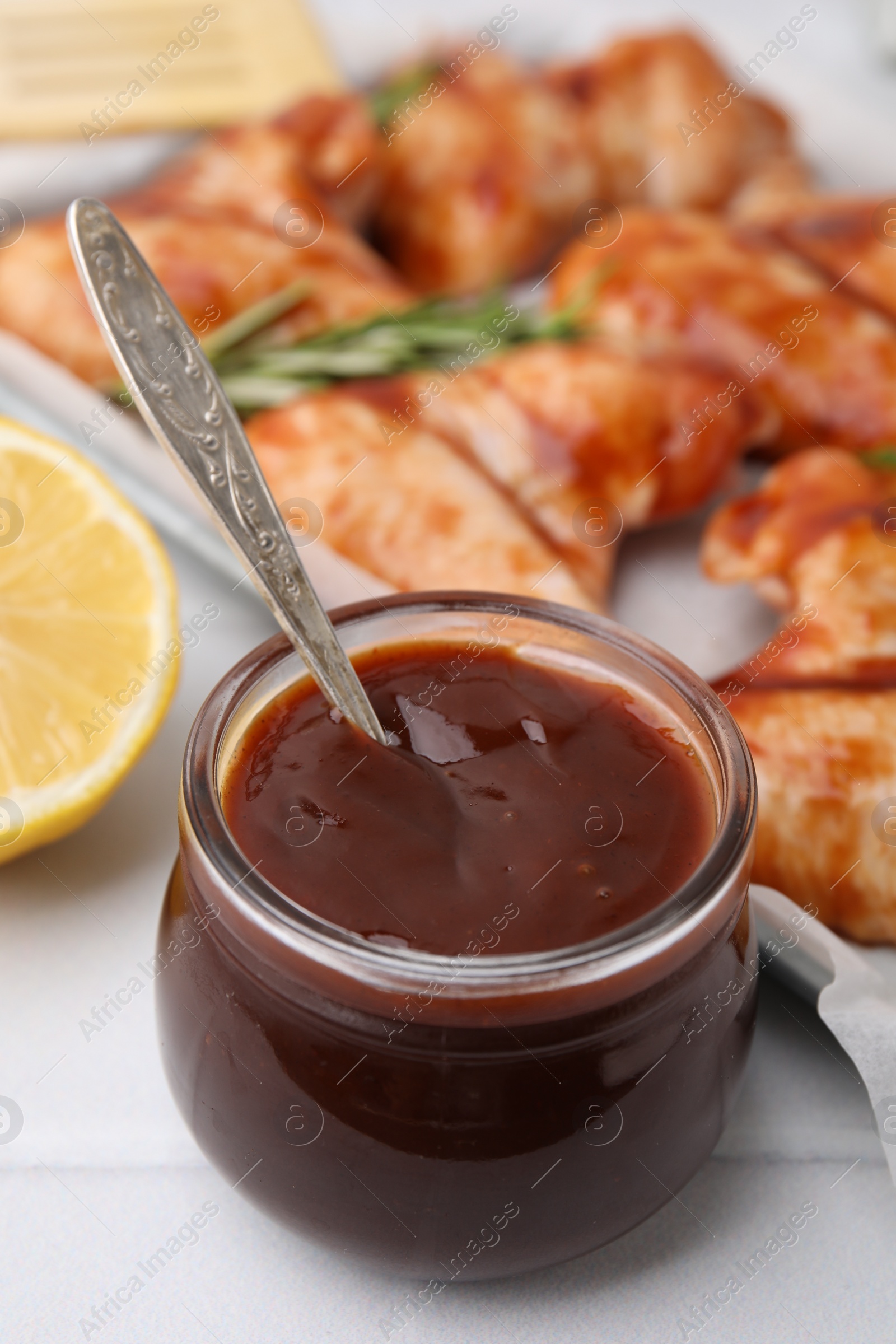 Photo of Fresh marinade with spoon in jar on light tiled table, closeup