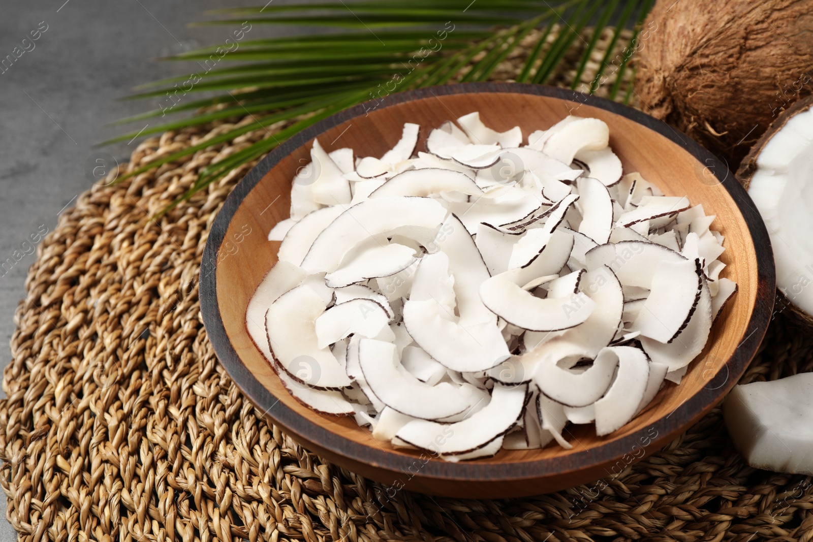 Photo of Tasty coconut chips in bowl on wicker mat