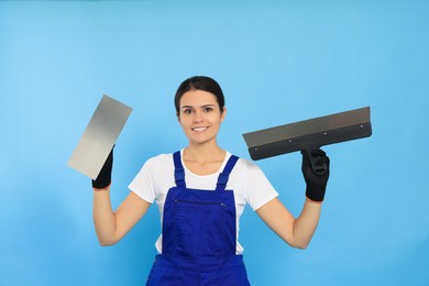 Professional worker with putty knives on light blue background