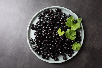 Plate with ripe blackcurrants and leaves on grey background, top view. Space for text