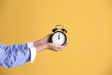 Young woman holding alarm clock on color background. Time concept