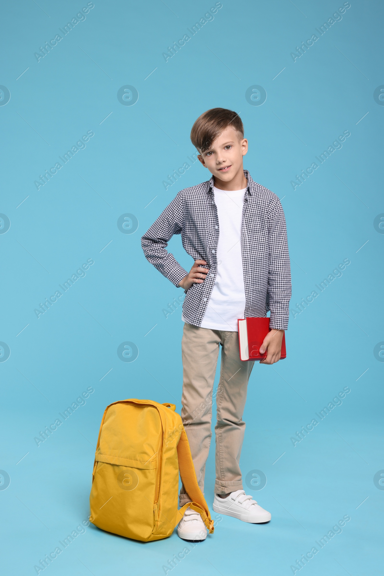 Photo of Cute schoolboy with book on light blue background