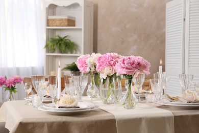 Stylish table setting with beautiful peonies and burning candles indoors