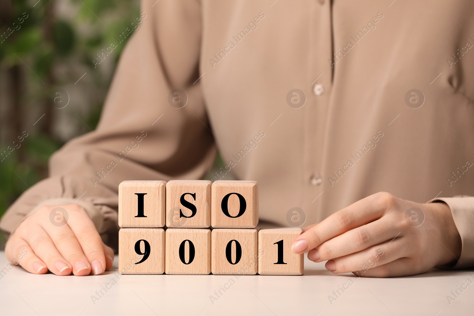 Photo of Woman making abbreviation ISO and number 9001 of wooden cubes at white table, closeup
