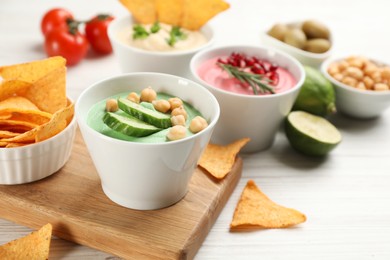 Photo of Different kinds of tasty hummus served with nachos on white wooden table, space for text