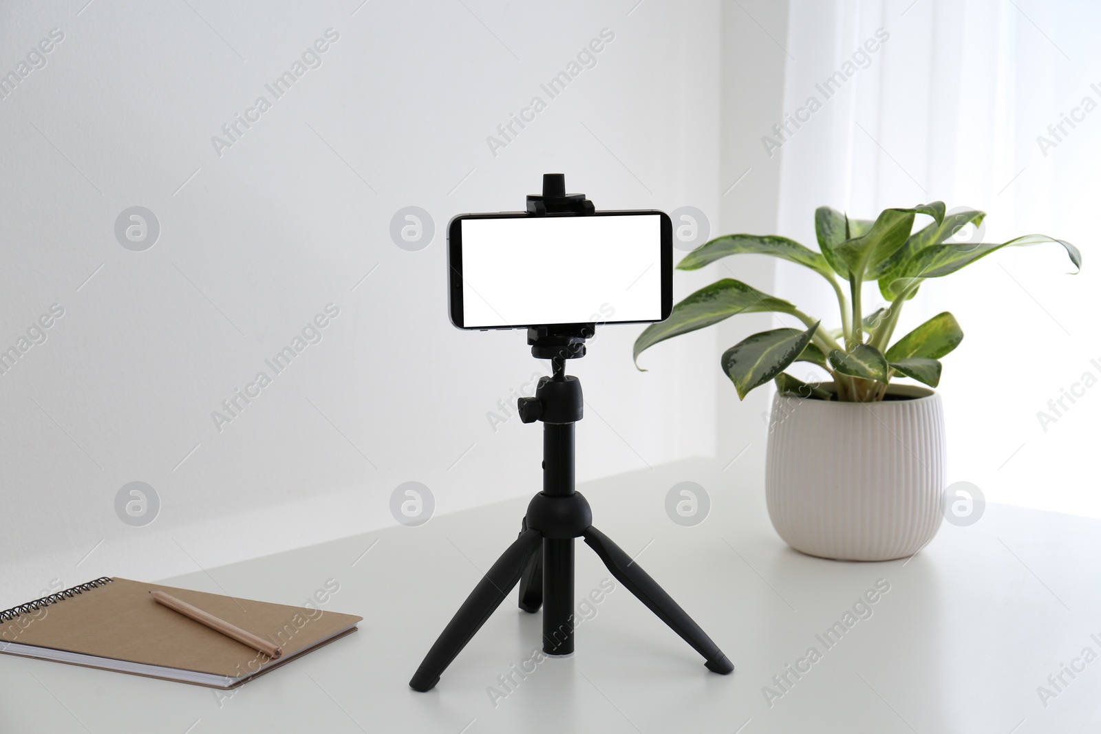 Photo of Smartphone with blank screen fixed to tripod on white table indoors. Mockup for design