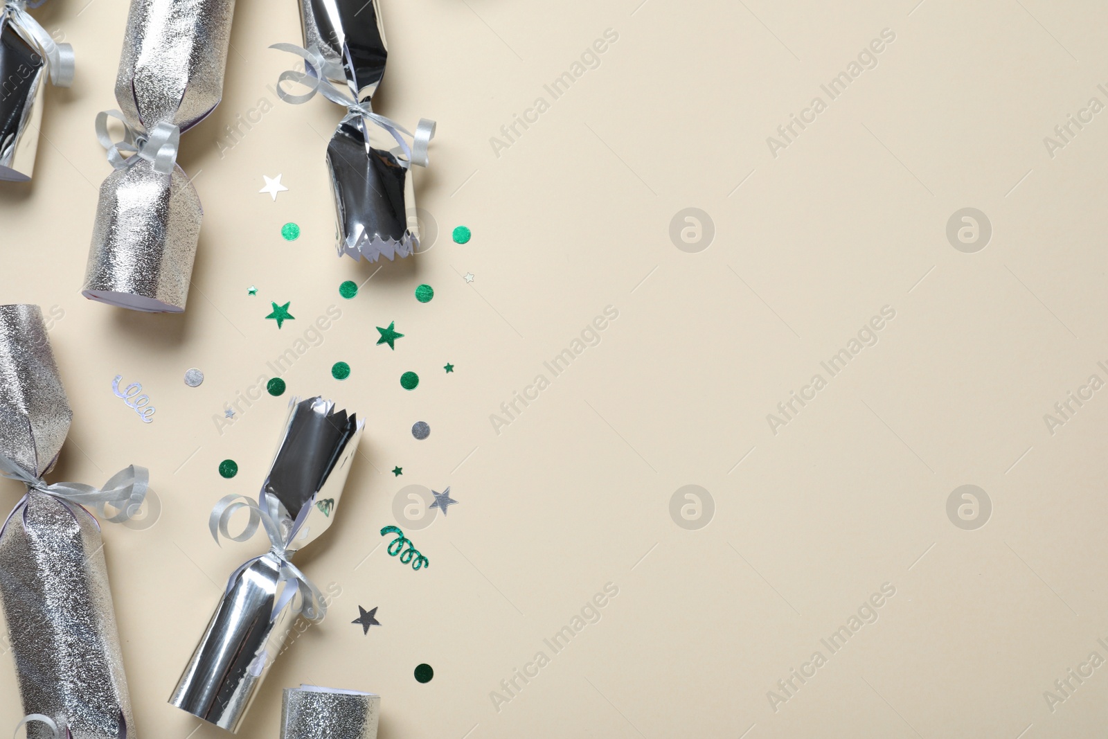 Photo of Open and closed silver Christmas crackers with shiny confetti on beige background, flat lay. Space for text