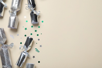 Photo of Open and closed silver Christmas crackers with shiny confetti on beige background, flat lay. Space for text