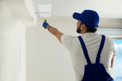 Photo of Handyman painting ceiling with white dye indoors, back view