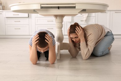 Photo of Scared mother with her son hiding under table in kitchen during earthquake