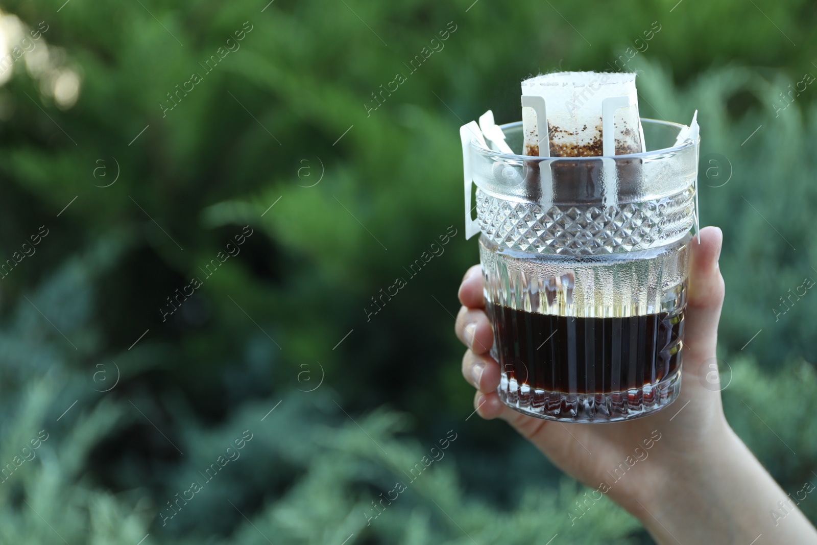 Photo of Woman holding glass with drip coffee bag outdoors, closeup. Space for text