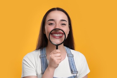 Happy woman holding magnifier glass near her face on yellow background