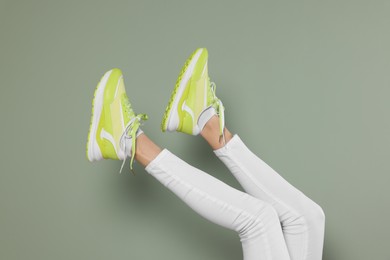 Woman wearing new stylish sneakers near light green background, closeup