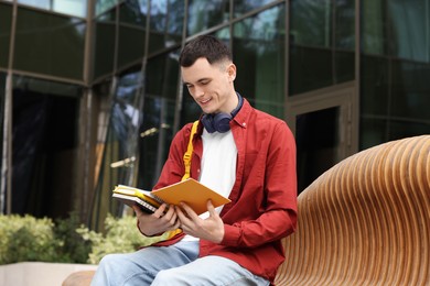 Photo of Happy young student studying with notebooks on bench outdoors