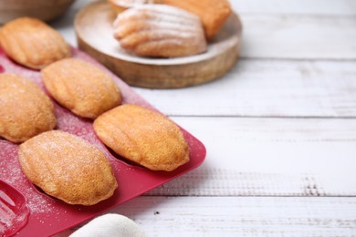 Photo of Delicious madeleine cookies and baking mold on white wooden table, closeup. Space for text
