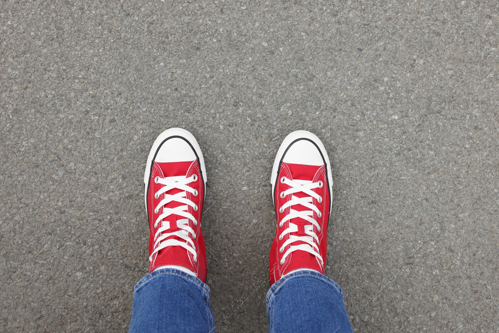 Photo of Woman in stylish gumshoes on asphalt, top view