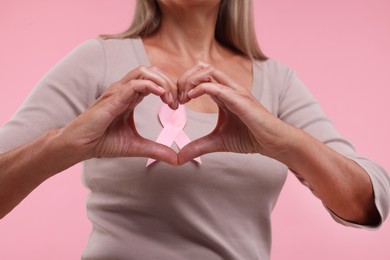 Woman with pink ribbon showing heart gesture on color background, closeup. Breast cancer awareness