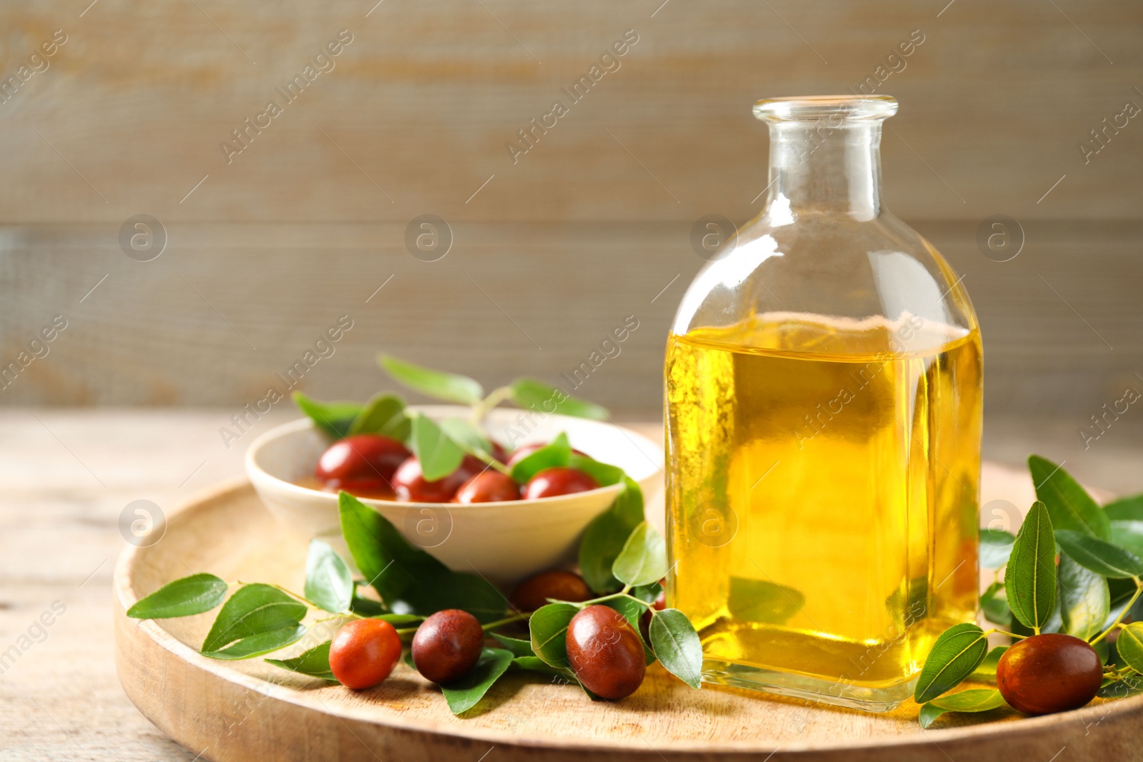 Photo of Glass bottle with jojoba oil and seeds on wooden table. Space for text