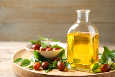 Glass bottle with jojoba oil and seeds on wooden table. Space for text