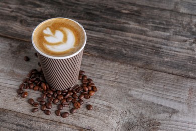 Coffee to go. Paper cup with tasty drink and roasted beans on wooden table, space for text