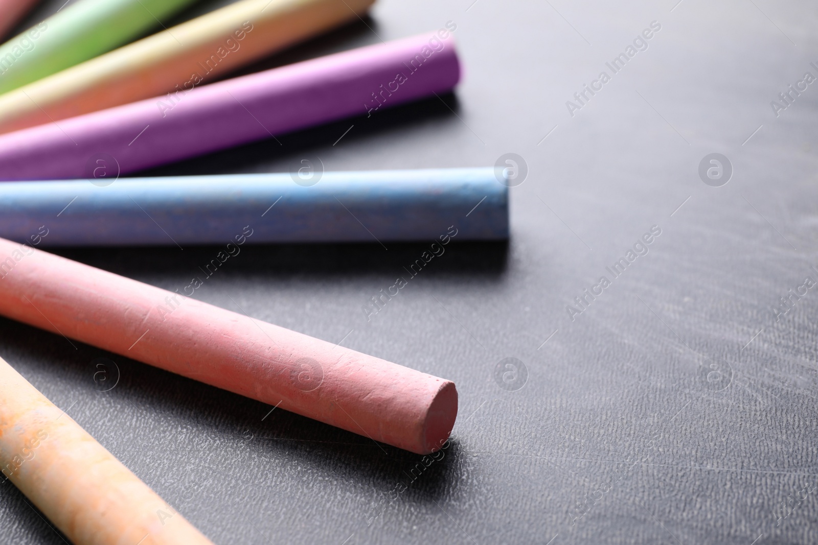 Photo of Pieces of color chalk on blackboard, closeup. Space for text