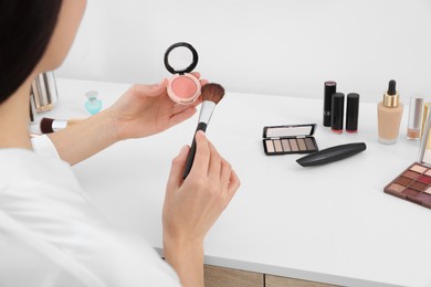 Photo of Woman with blusher and brush at dressing table indoors, closeup