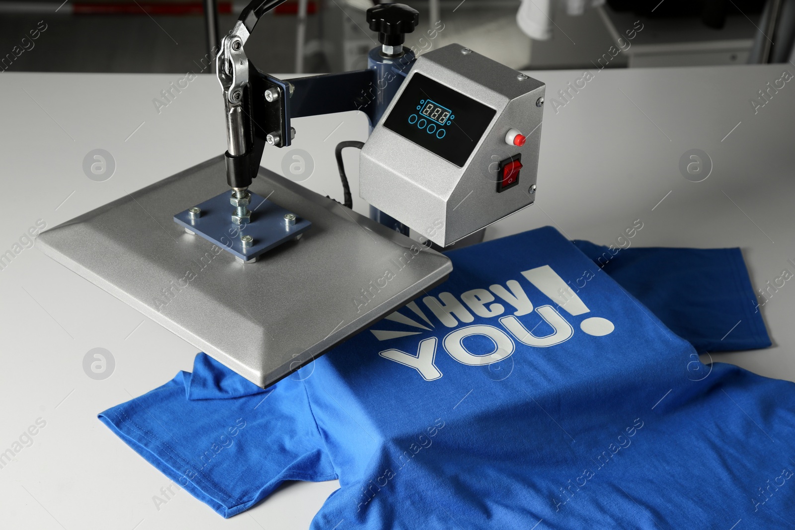 Photo of Printing logo. Heat press with blue t-shirt on white table