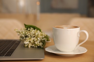 Cup of aromatic morning coffee, laptop and flowers on wooden table in cafe