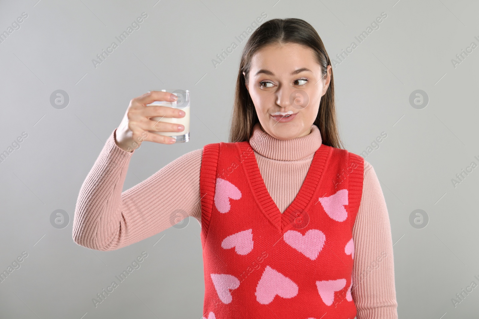 Photo of Happy woman with milk mustache holding glass of drink on light grey background