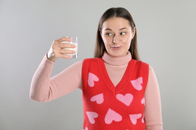 Happy woman with milk mustache holding glass of drink on light grey background