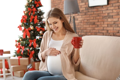 Photo of Pregnant woman near Christmas tree at home. Expecting baby