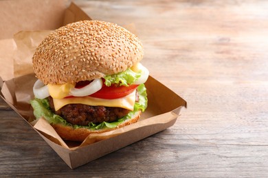Photo of Delicious burger in cardboard box on wooden table