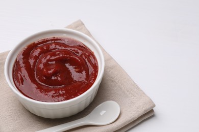 Photo of Organic ketchup in bowl and spoon on white table, space for text. Tomato sauce