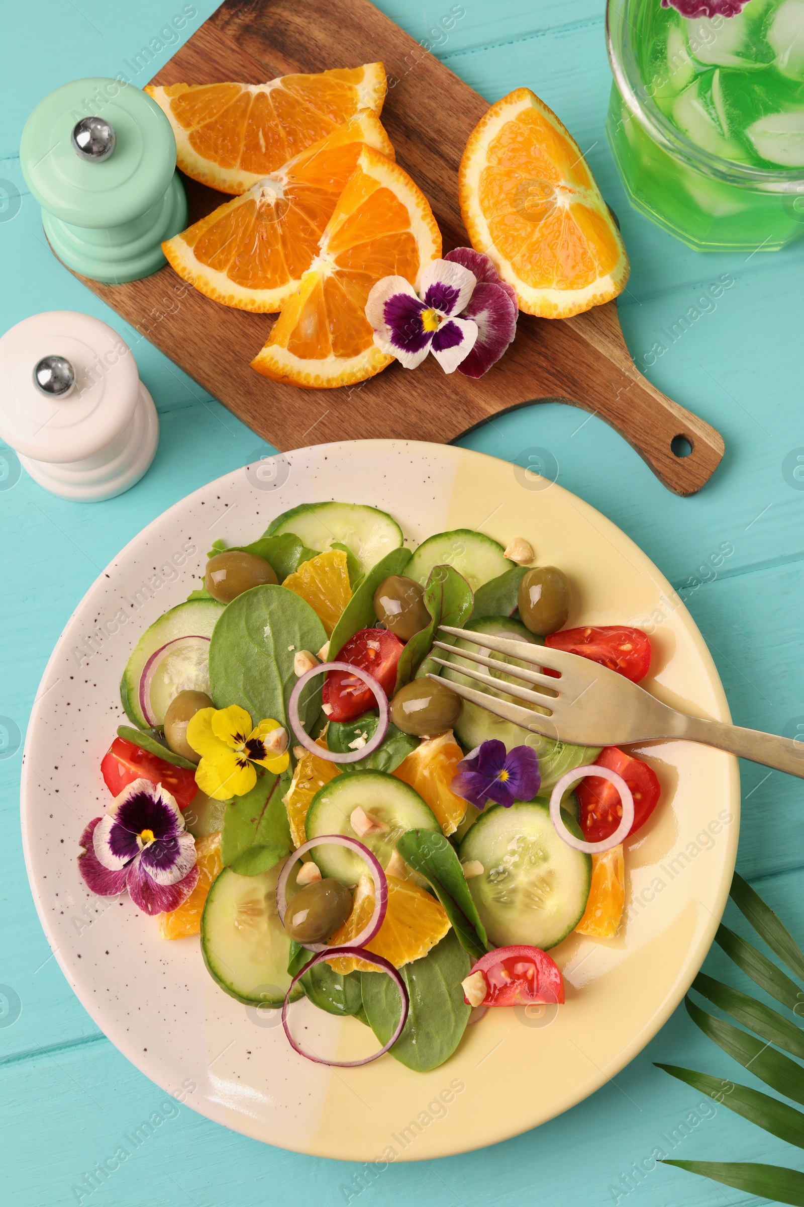 Photo of Delicious salad with orange, spinach, olives and vegetables served on turquoise wooden table, flat lay