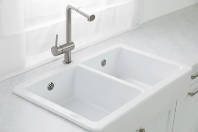 Photo of Modern sink and water tap near window in kitchen. Interior design