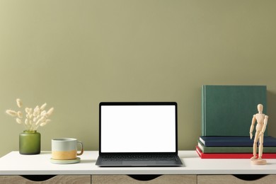 Stylish workplace with laptop, cup and vase of dry decorative spikes on white desk near olive wall indoors