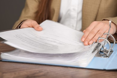 Businesswoman putting document into file folder at wooden table in office, closeup