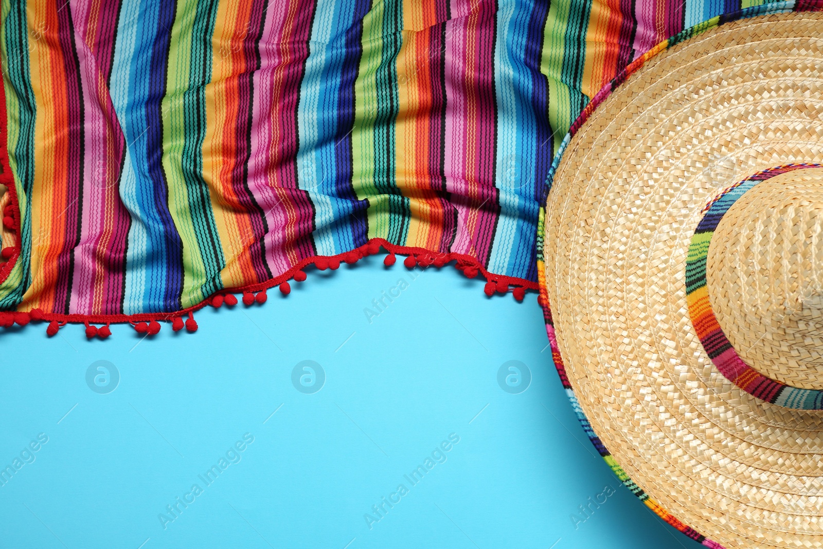 Photo of Mexican sombrero hat and colorful poncho on light blue background, flat lay. Space for text