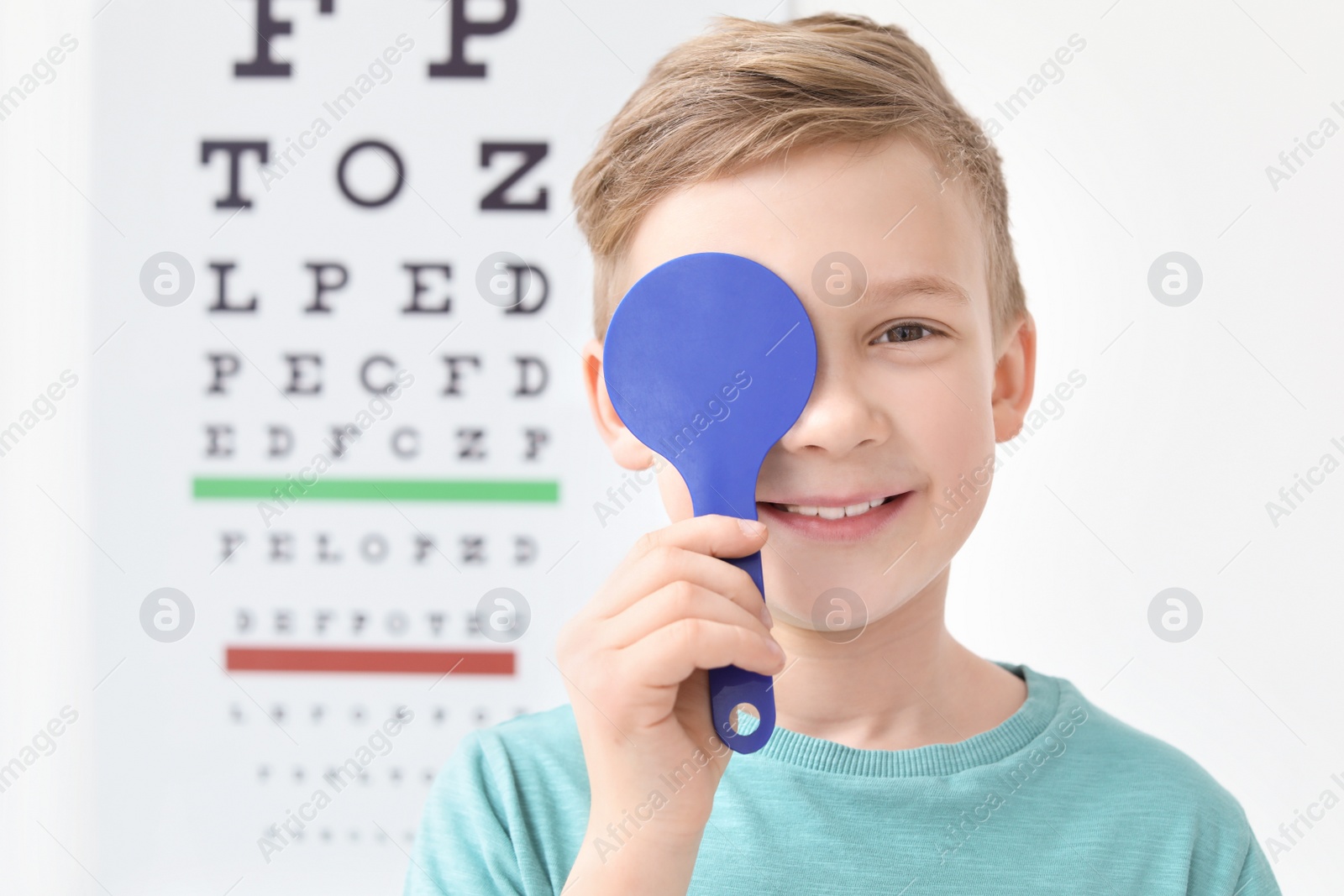 Photo of Cute little boy near eye chart in ophthalmologist office