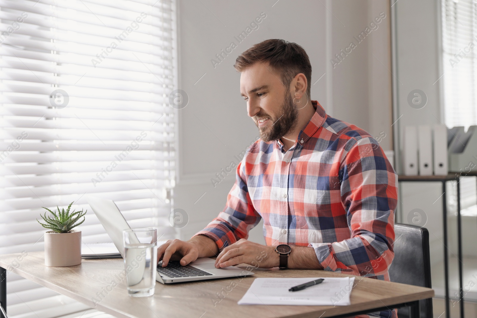 Photo of Young man working on laptop at table in office