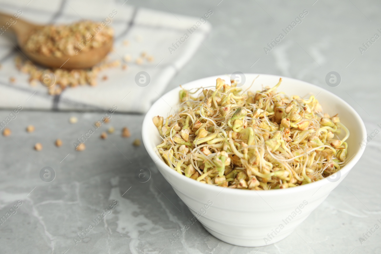 Photo of Bowl with sprouted green buckwheat on light grey table